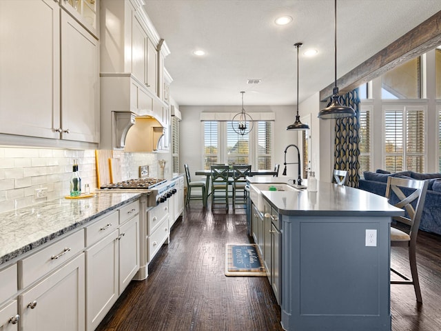 kitchen with hanging light fixtures, white cabinetry, a kitchen island with sink, and stainless steel gas stovetop