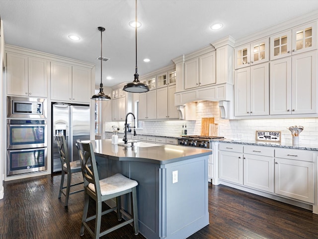 kitchen featuring sink, dark hardwood / wood-style floors, an island with sink, appliances with stainless steel finishes, and decorative light fixtures