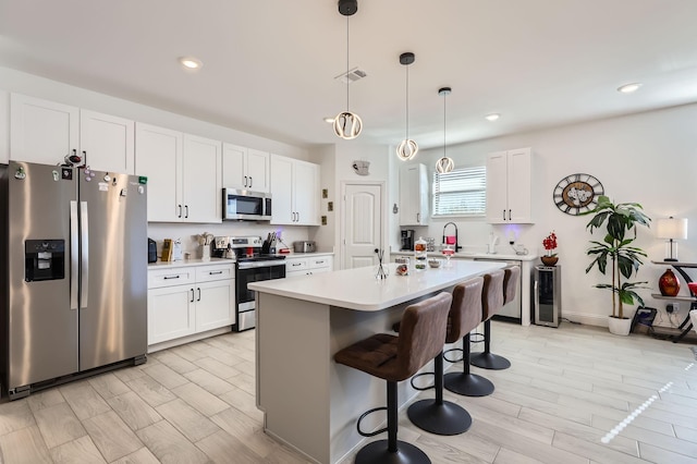 kitchen featuring appliances with stainless steel finishes, a breakfast bar, pendant lighting, a center island with sink, and white cabinetry