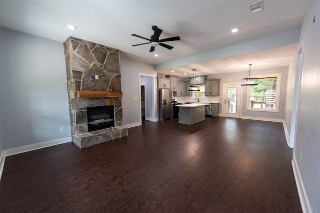 unfurnished living room featuring a stone fireplace, dark hardwood / wood-style floors, sink, and ceiling fan