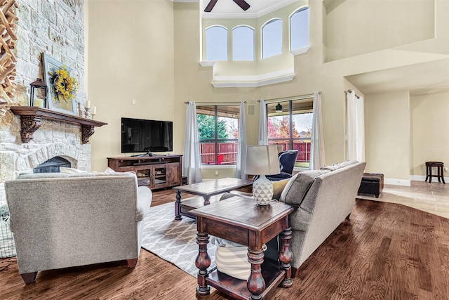 living room with hardwood / wood-style flooring, ceiling fan, a fireplace, and a high ceiling