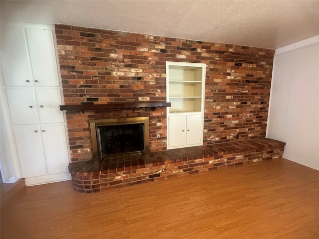 unfurnished living room featuring a textured ceiling, hardwood / wood-style flooring, and a brick fireplace