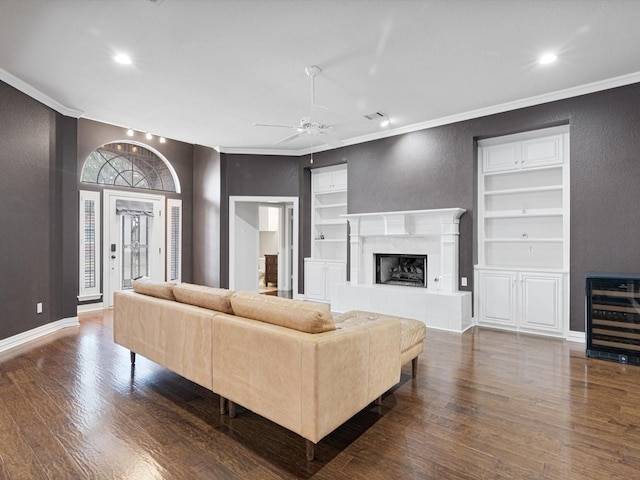 living room with dark wood-type flooring, a high end fireplace, ceiling fan, ornamental molding, and beverage cooler