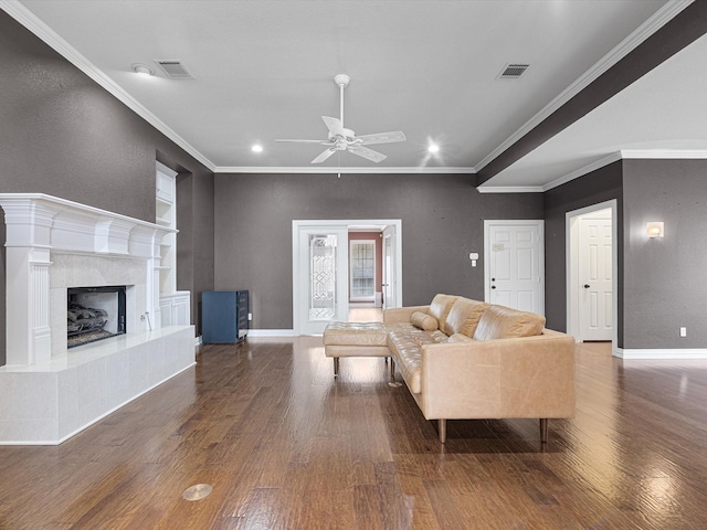 living room with dark hardwood / wood-style floors, ceiling fan, crown molding, and a tiled fireplace