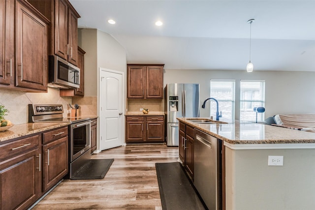 kitchen with decorative backsplash, appliances with stainless steel finishes, light wood-type flooring, sink, and a center island with sink