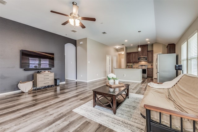 living room featuring ceiling fan, light wood-type flooring, sink, and vaulted ceiling