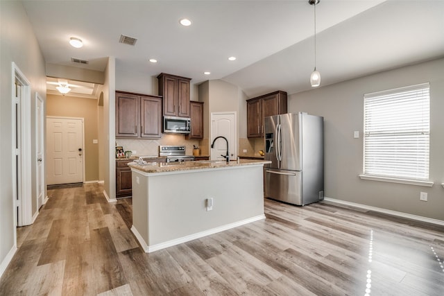 kitchen featuring light wood-type flooring, a kitchen island with sink, appliances with stainless steel finishes, and vaulted ceiling