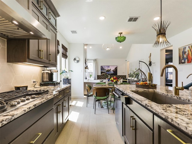 kitchen featuring sink, appliances with stainless steel finishes, dark brown cabinetry, decorative backsplash, and exhaust hood