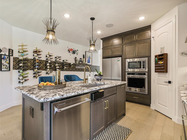 kitchen featuring appliances with stainless steel finishes, an island with sink, sink, hanging light fixtures, and light stone countertops