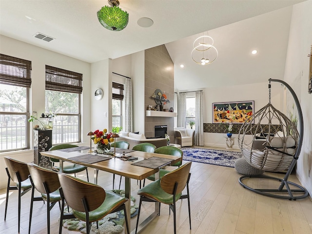 dining space featuring high vaulted ceiling, a tile fireplace, and light hardwood / wood-style flooring