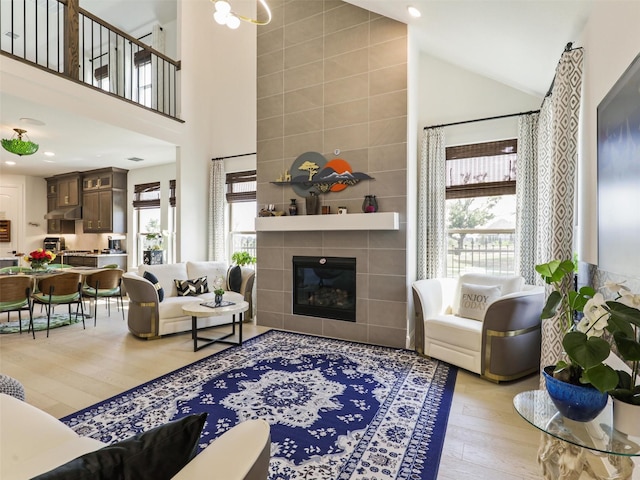 living room with a tile fireplace, plenty of natural light, high vaulted ceiling, and light hardwood / wood-style floors