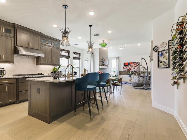 kitchen with light stone counters, light hardwood / wood-style flooring, dark brown cabinetry, and a center island with sink