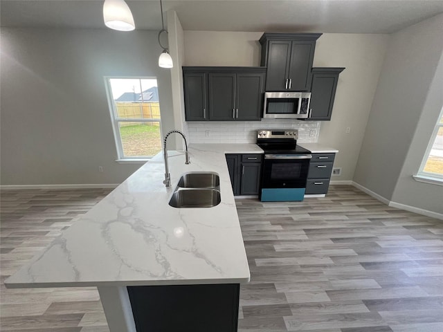 kitchen with appliances with stainless steel finishes, decorative light fixtures, sink, kitchen peninsula, and light stone countertops