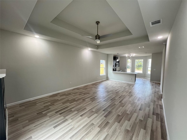 unfurnished living room featuring a raised ceiling, ceiling fan, and light hardwood / wood-style flooring