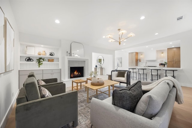 living room with a fireplace, built in shelves, light wood-type flooring, and a notable chandelier