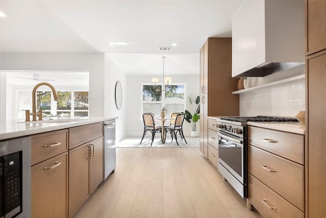 kitchen with plenty of natural light, wall chimney exhaust hood, stainless steel appliances, and light wood-type flooring