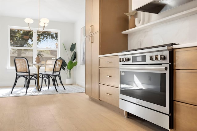 kitchen featuring pendant lighting, exhaust hood, stainless steel stove, light wood-type flooring, and a chandelier