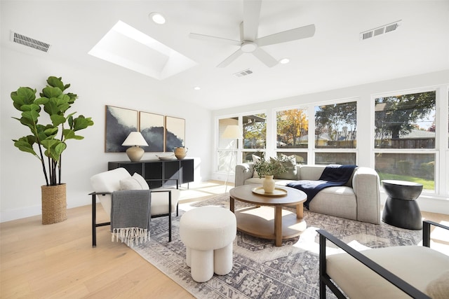 living room with ceiling fan, light hardwood / wood-style floors, a wealth of natural light, and a skylight