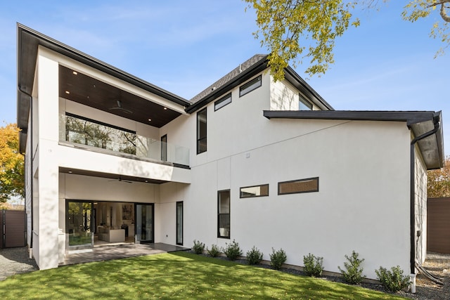 back of property with a balcony, ceiling fan, a patio area, and a lawn