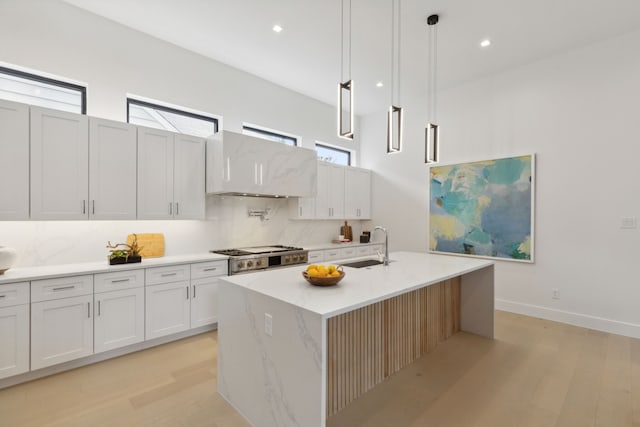 kitchen featuring a wealth of natural light, a center island with sink, extractor fan, and hanging light fixtures