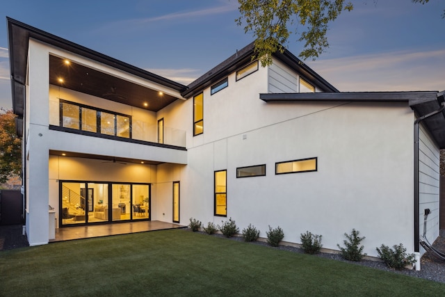 back house at dusk featuring a lawn and ceiling fan