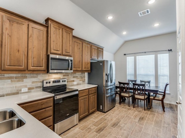 kitchen with decorative backsplash, appliances with stainless steel finishes, light wood-type flooring, sink, and lofted ceiling