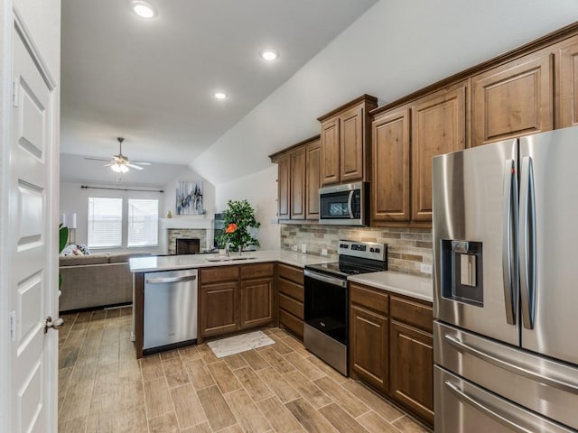 kitchen featuring lofted ceiling, ceiling fan, appliances with stainless steel finishes, backsplash, and kitchen peninsula