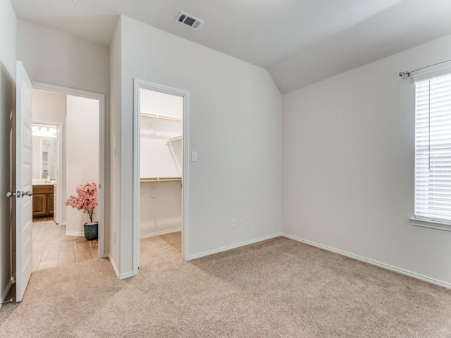 unfurnished bedroom featuring light colored carpet, a spacious closet, vaulted ceiling, and a closet