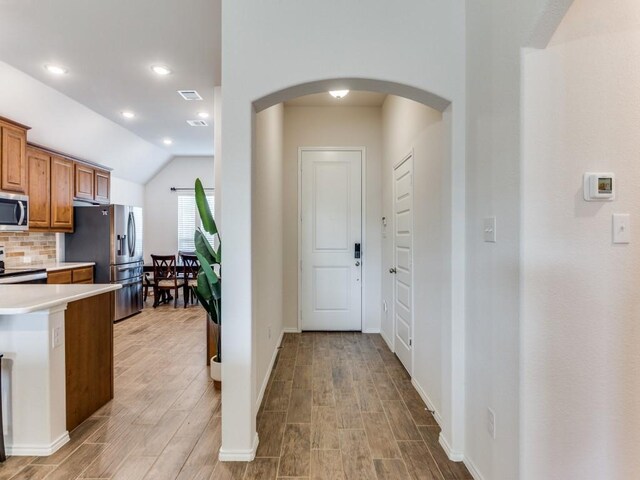 kitchen featuring light hardwood / wood-style floors, vaulted ceiling, appliances with stainless steel finishes, and tasteful backsplash