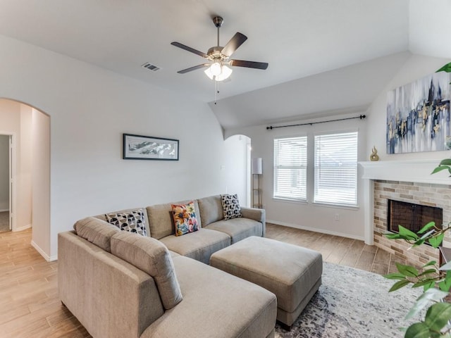 living room featuring a brick fireplace, light wood-type flooring, vaulted ceiling, and ceiling fan