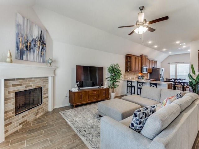 living room featuring ceiling fan, a fireplace, lofted ceiling, and light wood-type flooring