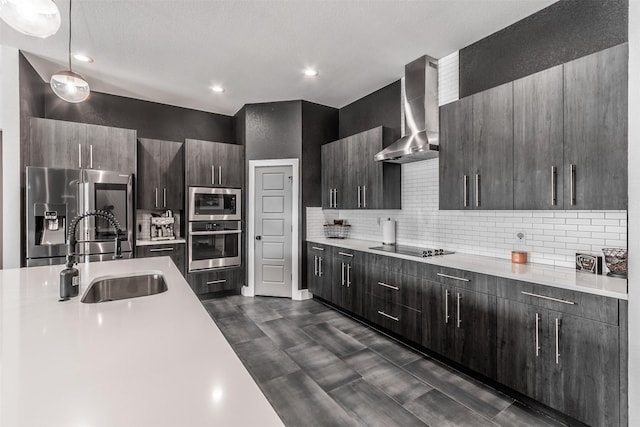 kitchen with backsplash, wall chimney exhaust hood, stainless steel appliances, sink, and hanging light fixtures