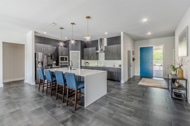 kitchen with a center island with sink, wall chimney range hood, sink, a kitchen bar, and stainless steel appliances