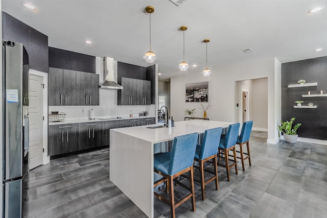 kitchen with a kitchen breakfast bar, wall chimney exhaust hood, sink, a center island with sink, and stainless steel refrigerator