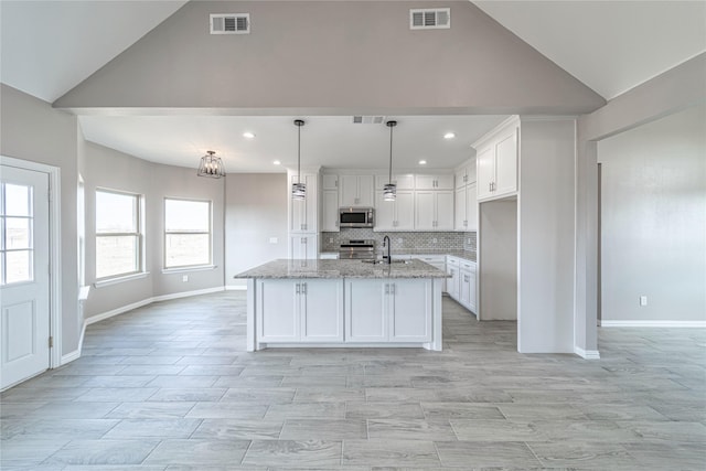 kitchen with pendant lighting, light stone counters, white cabinetry, and appliances with stainless steel finishes