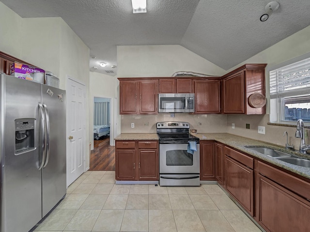 kitchen featuring sink, vaulted ceiling, a textured ceiling, light tile patterned floors, and stainless steel appliances