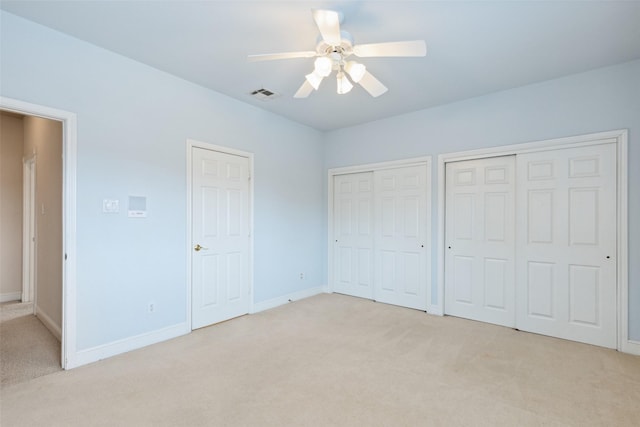 unfurnished bedroom featuring multiple closets, ceiling fan, and light colored carpet