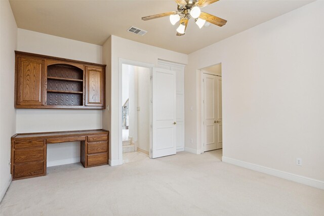 unfurnished office with ceiling fan, light colored carpet, and built in desk