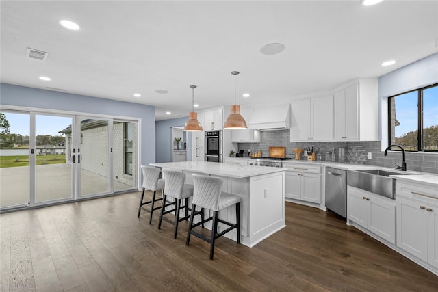 kitchen featuring stainless steel appliances, a center island, a healthy amount of sunlight, and decorative light fixtures