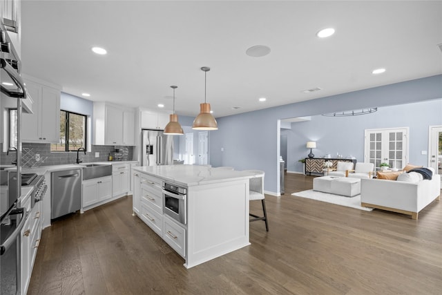 kitchen featuring appliances with stainless steel finishes, dark wood-type flooring, pendant lighting, white cabinets, and a center island