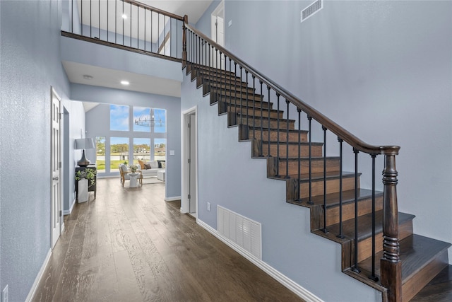 stairway with hardwood / wood-style floors, a high ceiling, and an inviting chandelier