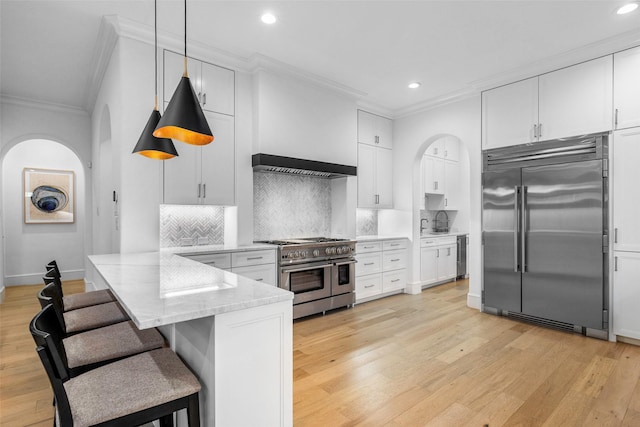 kitchen with kitchen peninsula, a kitchen breakfast bar, premium appliances, decorative light fixtures, and white cabinetry