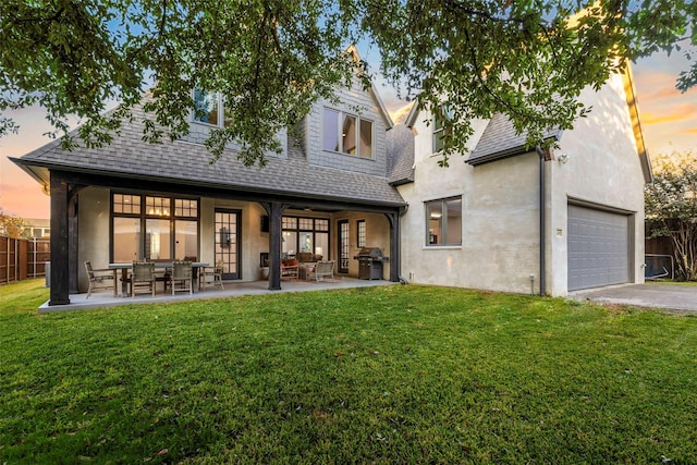 back house at dusk featuring a lawn and a patio area