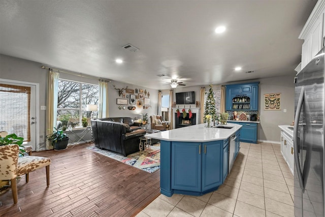 kitchen with visible vents, an island with sink, freestanding refrigerator, light countertops, and blue cabinetry