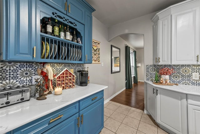 kitchen with blue cabinets, light tile patterned floors, white cabinetry, and arched walkways