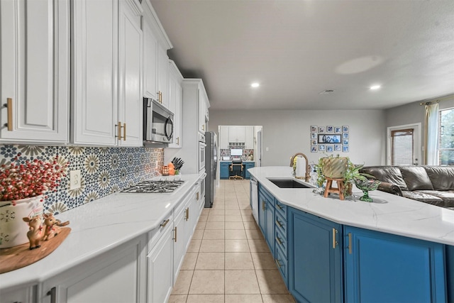 kitchen featuring blue cabinets, stainless steel appliances, a sink, white cabinets, and open floor plan