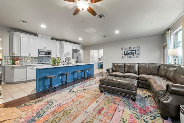 living room featuring ceiling fan, light wood-type flooring, visible vents, and recessed lighting