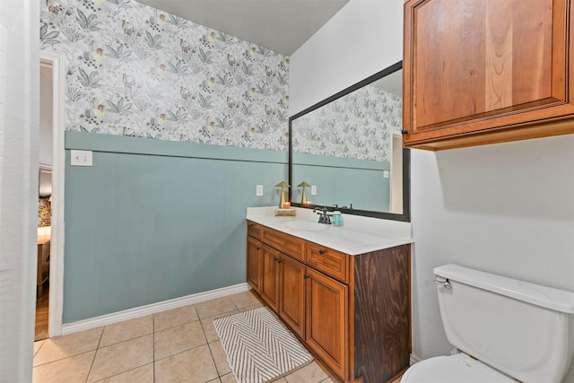 bathroom featuring toilet, vanity, wainscoting, tile patterned floors, and wallpapered walls