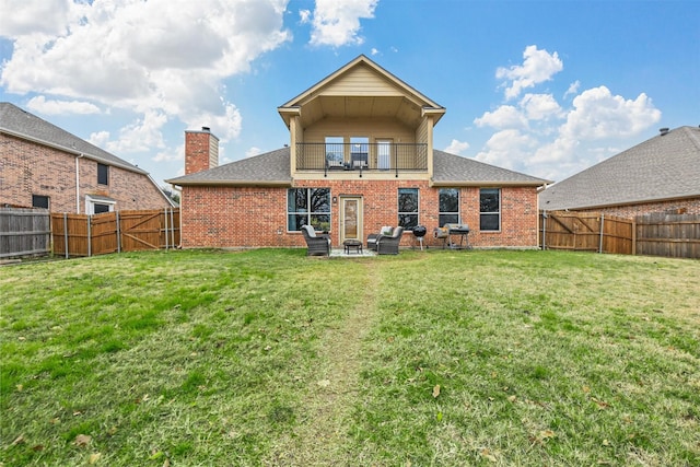 rear view of house featuring a balcony, a fenced backyard, a lawn, and brick siding