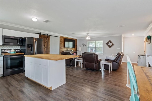 kitchen featuring appliances with stainless steel finishes, butcher block countertops, backsplash, white cabinets, and a barn door